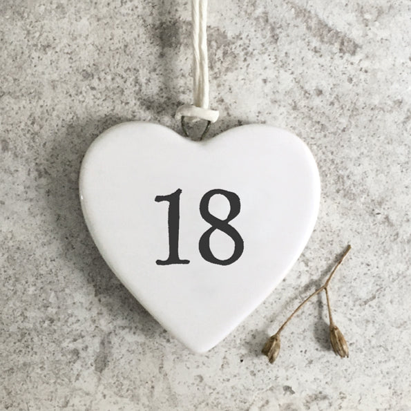 Heart-shaped white ornament with the number 18 on a textured gray surface