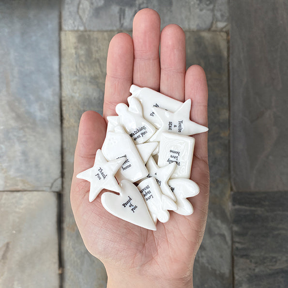 Hand holding white ceramic stars with text against a stone wall background