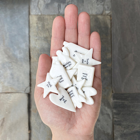 Hand holding white ceramic stars with text against a stone wall background