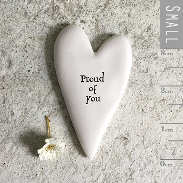 Heart-shaped ceramic item with 'Proud of you' text on a textured surface.