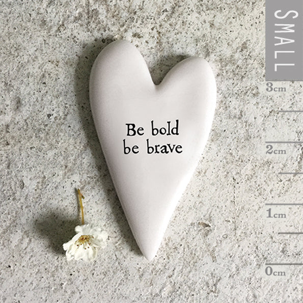 Heart-shaped ceramic piece with 'Be bold be brave' text on a textured surface with a flower and ruler for scale.