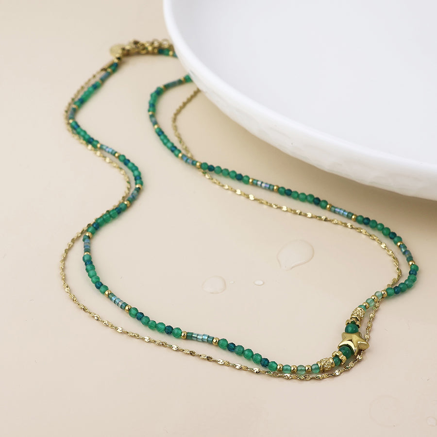 Double stranded green beaded necklace with gold chain and star charm on a beige surface