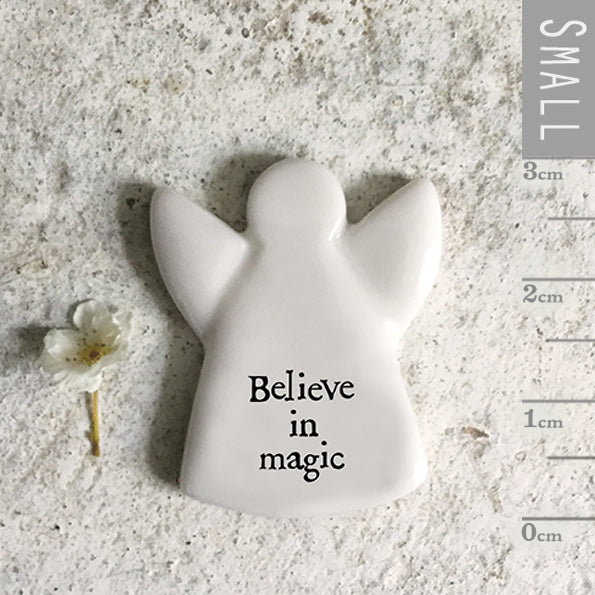 Small angel figurine with 'Believe in magic' text on a sandy surface with a white flower.