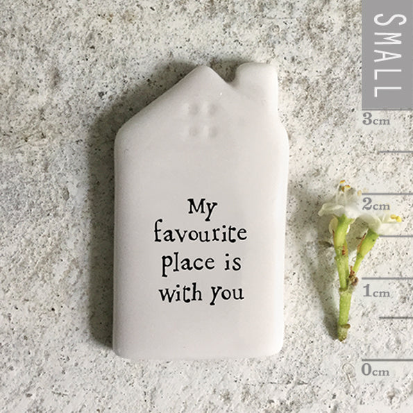 Small white ceramic house-shaped object with 'My favourite place is with you' text, next to a flower and ruler for scale on a textured surface.