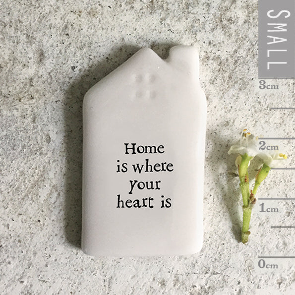 Small white ceramic house-shaped object with 'home is where your heart is' text on a textured surface with a ruler for scale.