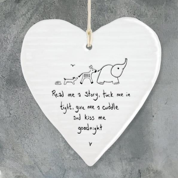 A white ceramic hanging heart with a graphic of a baby and an elephant, and text that reads 'Read me a story, tickle me, give me a cuddle and a kiss - goodnight'.