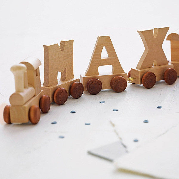 Wooden letters with small wheels spelling MAX with a wooden train attached to the front. Image has a white background 